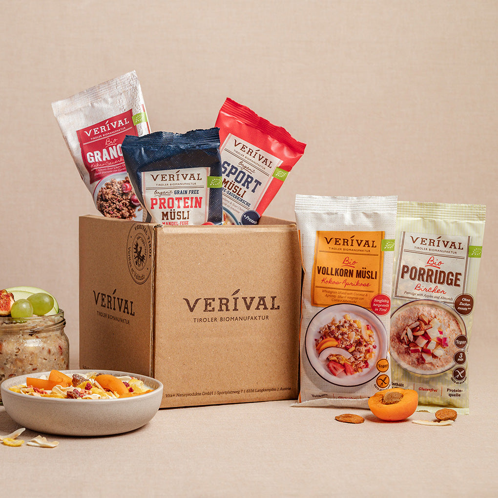A box with the label “Verival” on it, surrounded by various Verival muesli and porridge packages as well as bowls of ready-made muesli and fruit.