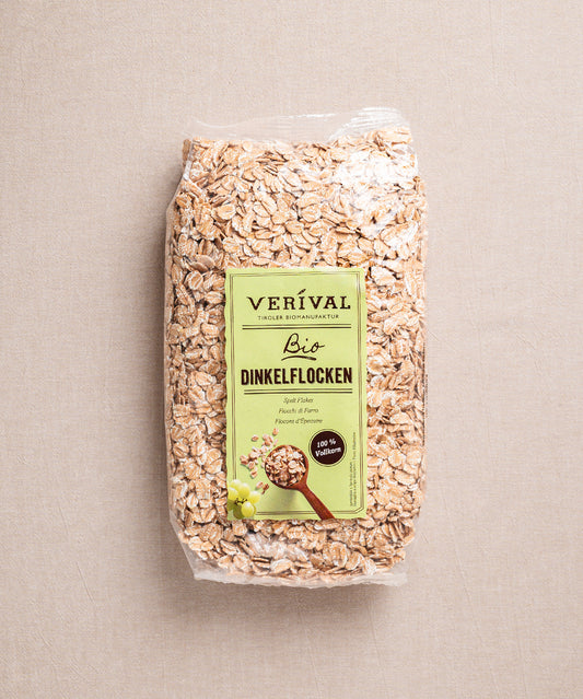 Eine Packung Dinkelflocken von Verival Bio, perfekt für ein vollwertiges Frühstück, wird in einem transparenten Beutel geliefert, auf dem die an komplexen Kohlenhydraten reichen Dinkelflocken abgebildet sind.