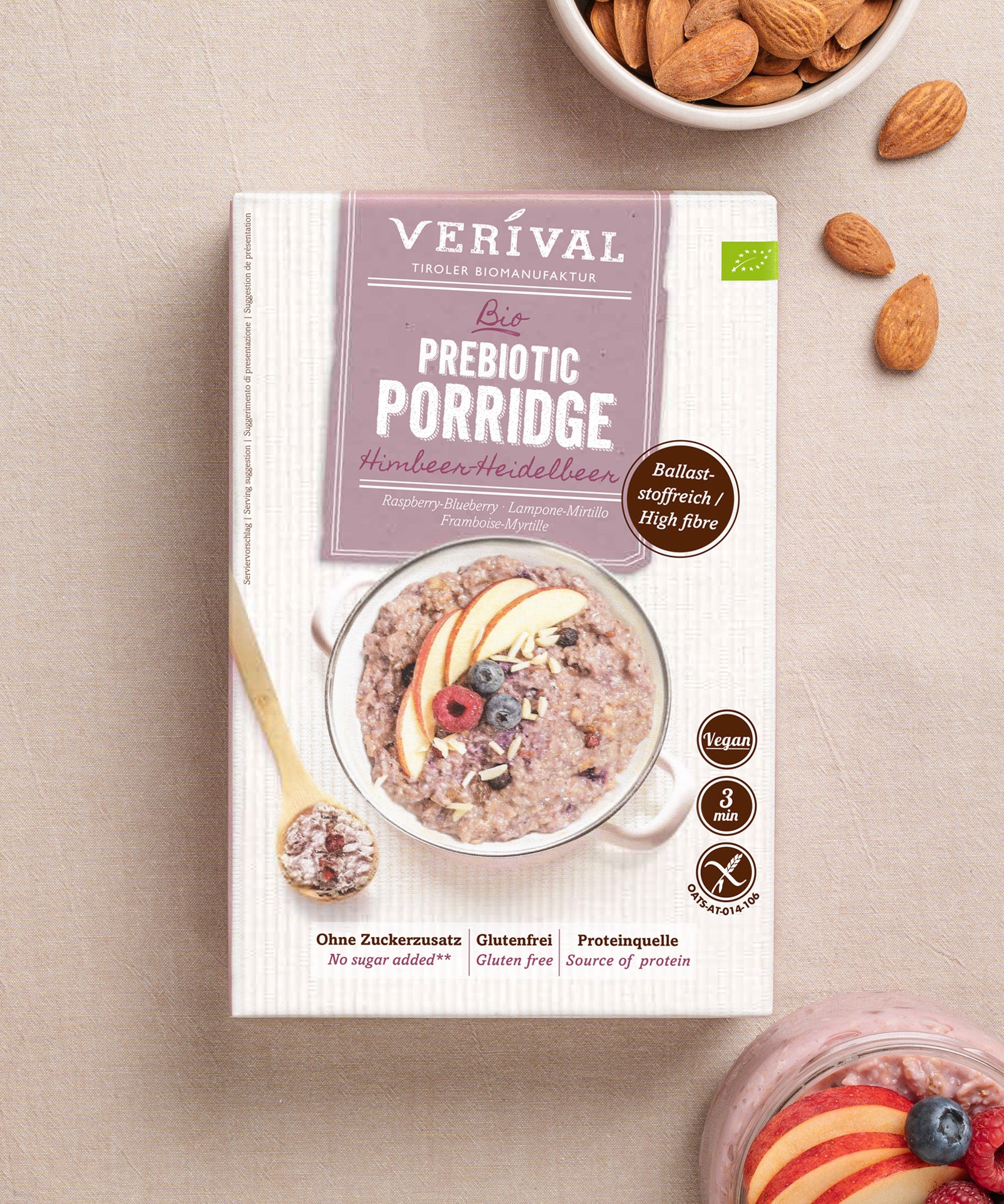 Eine Schachtel Prebiotic Porridge Himbeer-Heidelbeer von Verival Bio, umgeben von Mandeln. Die Verpackung zeigt Porridge mit Fruchtscheiben und betont dessen veganen Charakter, reich an Ballaststoffen, frei von Zuckerzusatz und mit nur 3 Minuten Zubereitungszeit.
