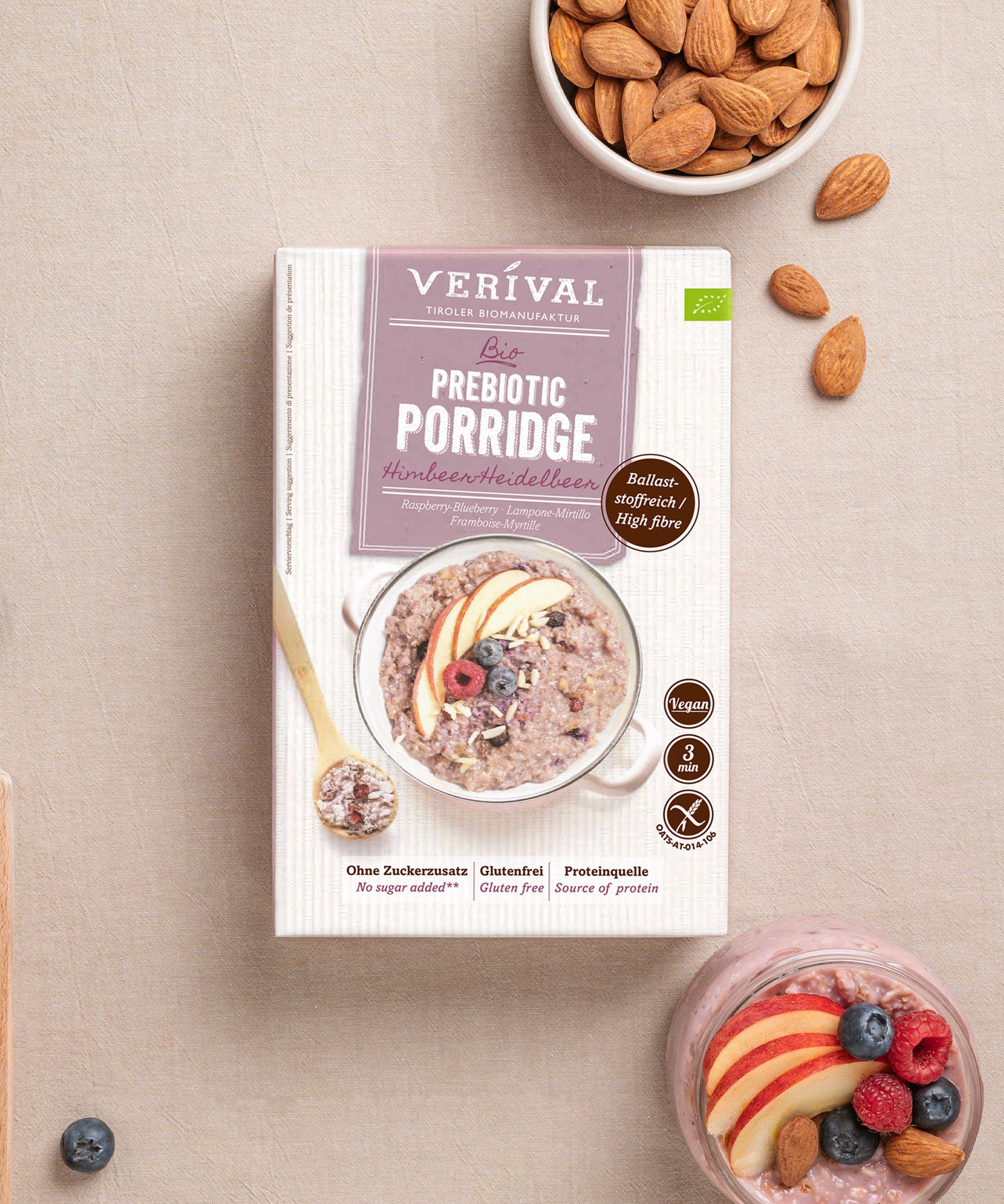Eine Packung Prebiotischer Porridge Himbeer-Heidelbeer von Verival Bio neben einer Schüssel Porridge mit Apfelscheiben und Beeren, verstreuten Mandeln und einzelnen Beeren auf hellem Untergrund. Die Verpackung betont die vegane, glutenfreie und proteinreiche Variante sowie die darmfreundlichen Ballaststoffe für deine Darmflora.