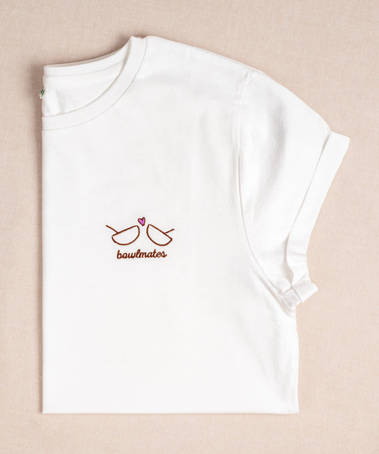Das Verival Bio T-Shirt Bowlmates ist ein weißes Shirt aus Baumwolle mit einer roten Stickerei von zwei handgezeichneten Gläsern und einem kleinen Herzen mit der Aufschrift „Bowlmates“ auf beigem Hintergrund, ideal für Frühstücksliebhaber.