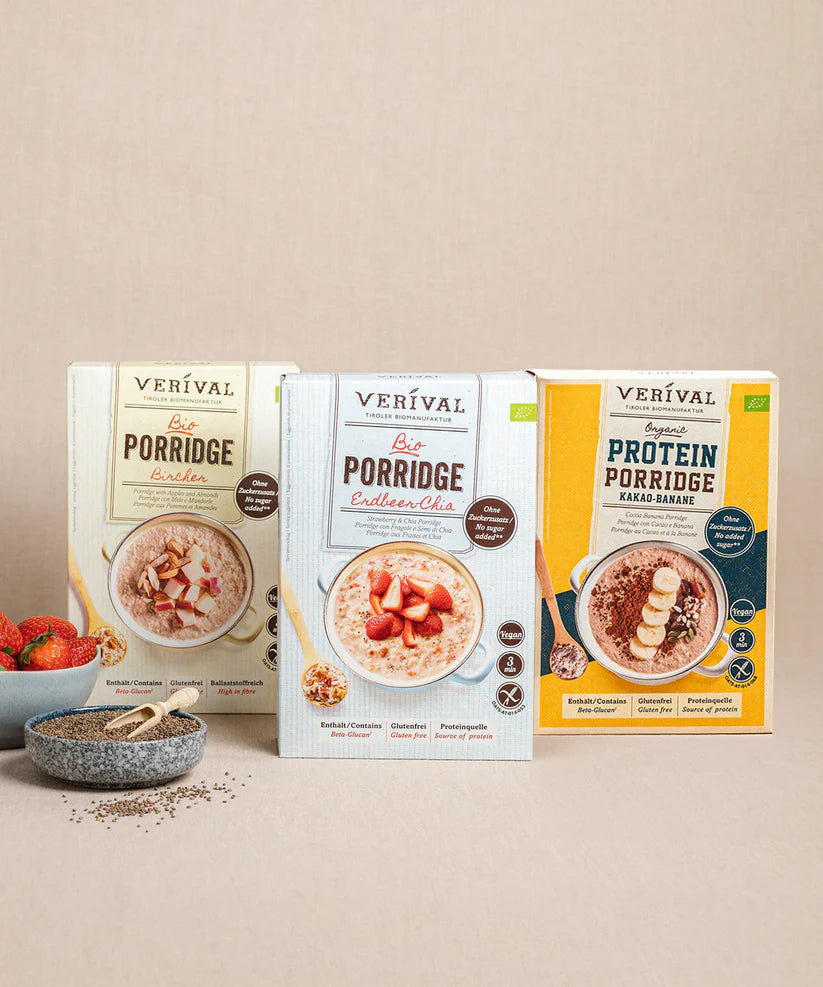 Das Porridge Stars Probierpaket von Verival Bio mit Bestseller-Geschmacksrichtungen wie Bircher, Erdbeer-Chia und Protein Kakao-Banane wird geschmackvoll mit einer Schüssel Porridge, garniert mit Chiasamen und Erdbeeren präsentiert.
