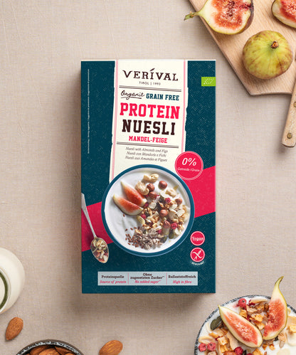 Eine Packung Verival Bio Bio Mandel-Feige Grain Free Protein Nüsli, umgeben von frischen Feigen, Nüssen und Schalen mit Müsli.