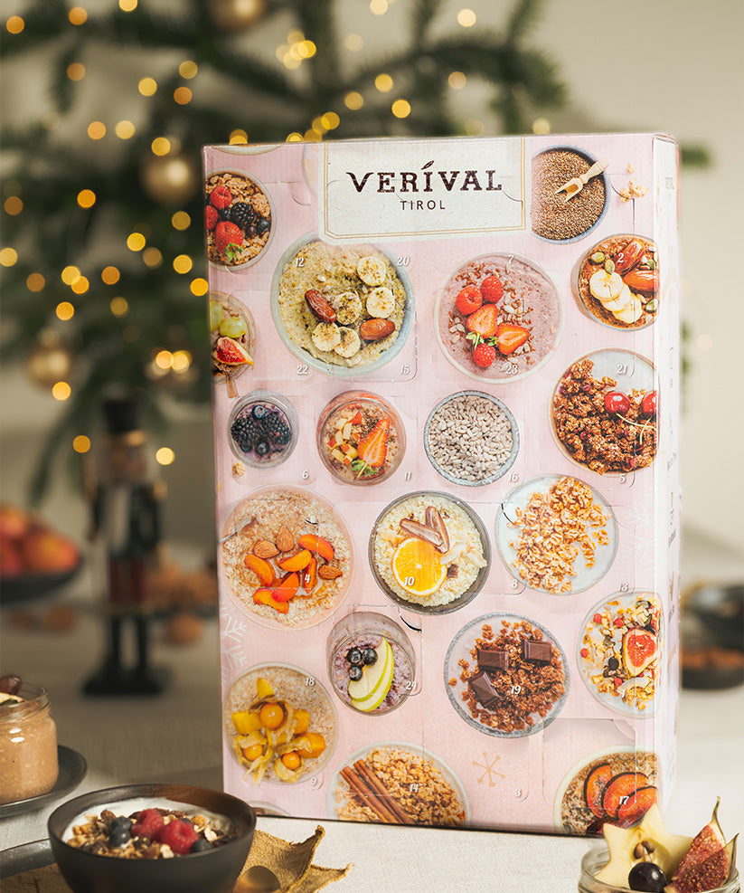 Entdecken Sie die Adventskalender-Box Vegan von Verival Bio. Hinter den 24 Fenstern verbergen sich Bio-Frühstücks-Leckereien. Ein charmanter Nussknacker und Weihnachtsdekorationen zieren diese festliche Box vor dem Hintergrund eines verschwommenen Weihnachtsbaums und funkelnder Lichter – perfekt für vegane Feiertage.